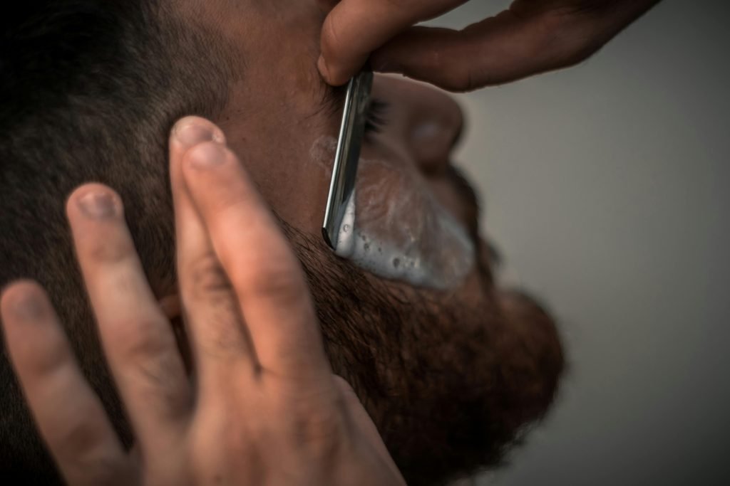 pexels-photo-1319461-1319461 Detailed close-up image of a barber using a razor for precise beard trimming in the barbershop.